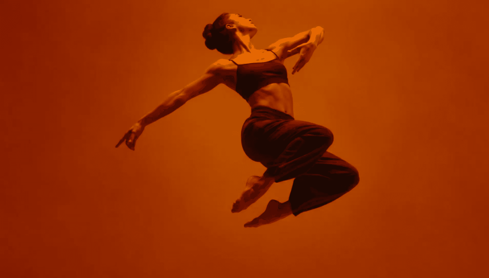 Dancer suspended mid-leap, lit in warm ember light