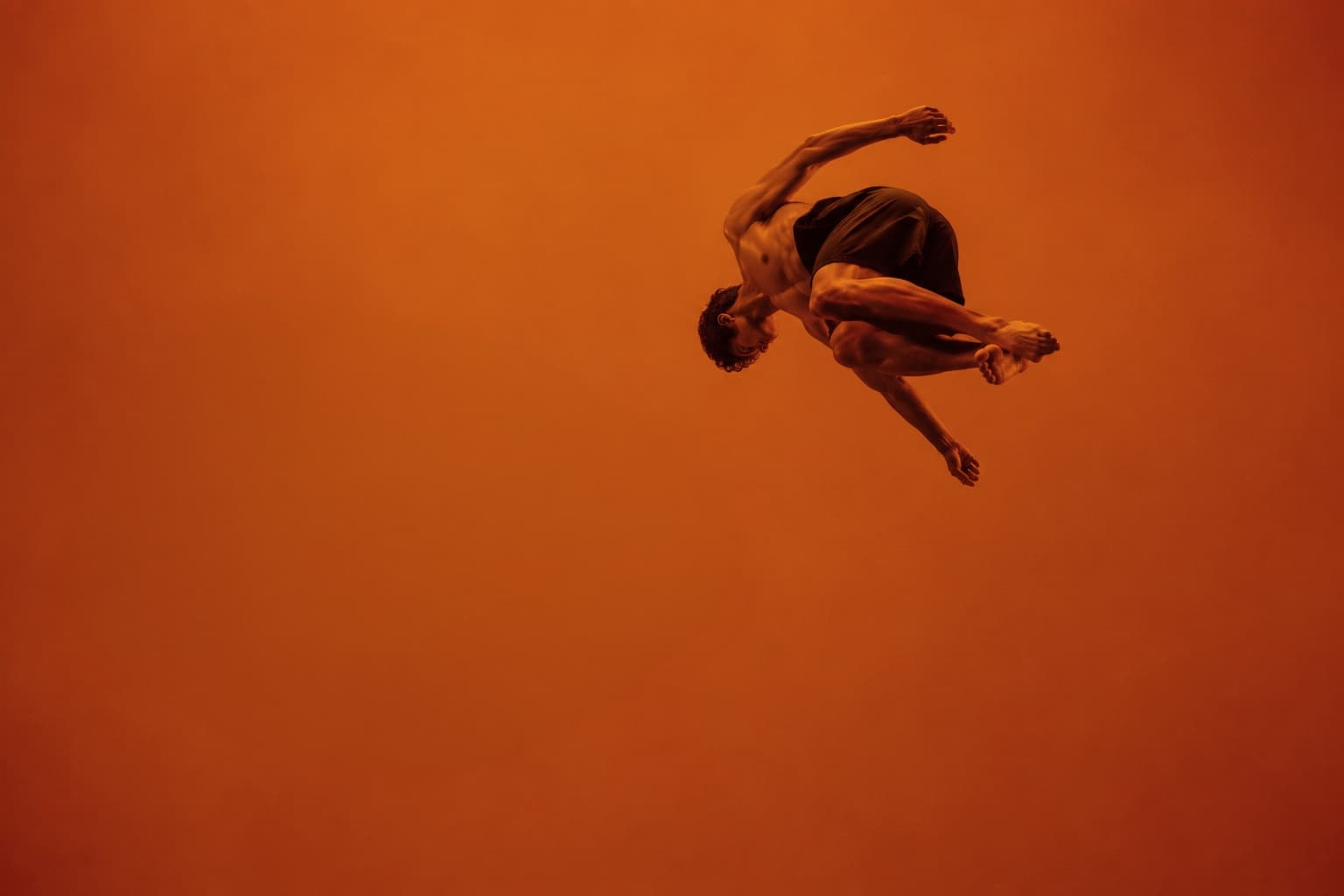 Dancer tumbling mid-air against a deep orange field